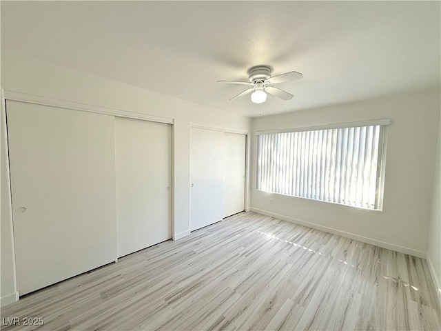 unfurnished bedroom featuring baseboards, multiple closets, ceiling fan, and light wood finished floors