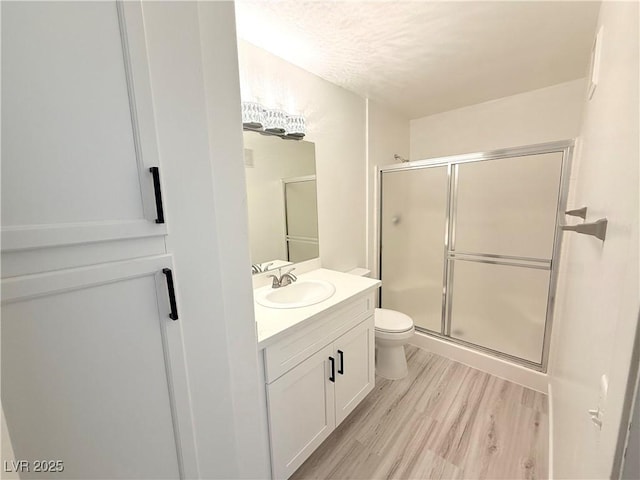 full bath featuring vanity, toilet, wood finished floors, and a stall shower