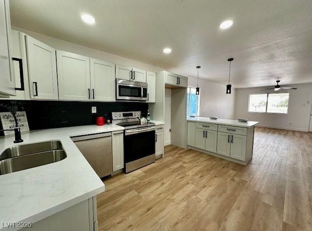 kitchen featuring backsplash, ceiling fan, light wood-style floors, stainless steel appliances, and a sink