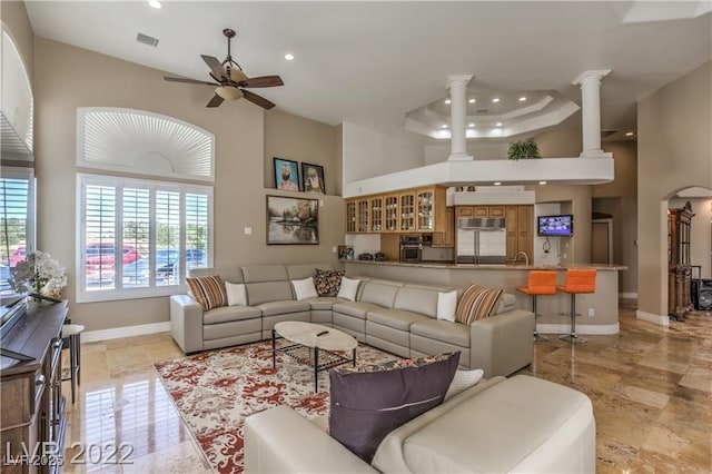 living room with visible vents, a ceiling fan, a high ceiling, decorative columns, and baseboards