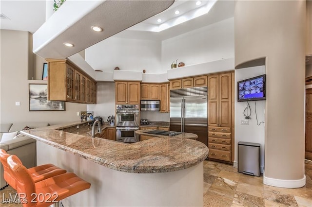 kitchen with glass insert cabinets, light stone countertops, brown cabinets, a peninsula, and stainless steel appliances