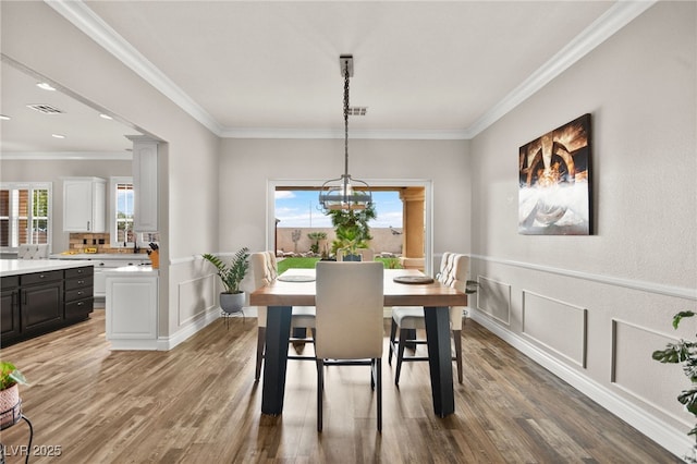 dining space featuring visible vents, wood finished floors, a chandelier, and crown molding