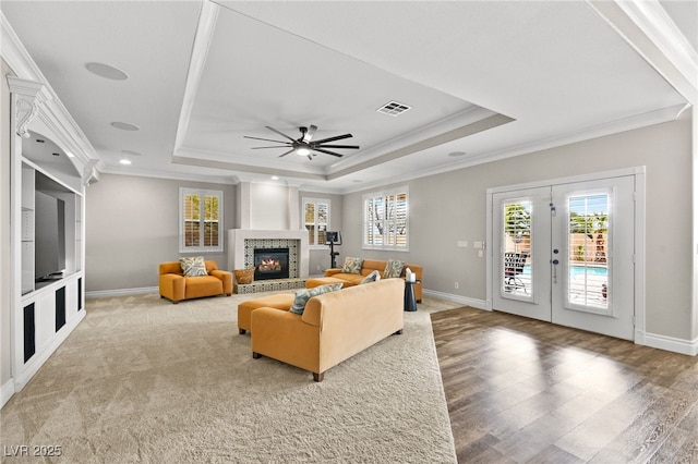 living area featuring visible vents, ornamental molding, a raised ceiling, and a glass covered fireplace