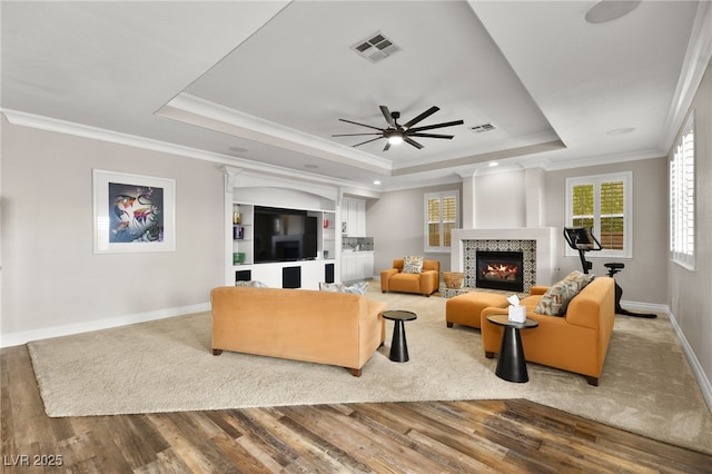 living area featuring a raised ceiling, a tile fireplace, visible vents, and ceiling fan