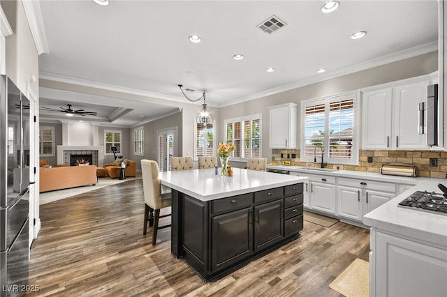 kitchen with visible vents, a warm lit fireplace, wood finished floors, white cabinetry, and light countertops