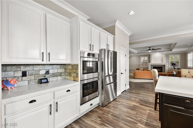 kitchen with crown molding, light countertops, a warm lit fireplace, appliances with stainless steel finishes, and white cabinets