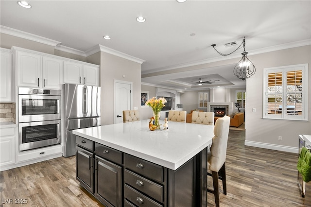 kitchen with a kitchen bar, light wood-style flooring, a warm lit fireplace, white cabinetry, and appliances with stainless steel finishes