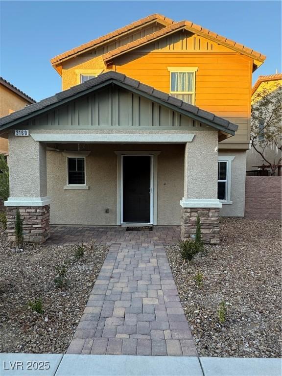 rear view of property featuring board and batten siding, stone siding, and stucco siding