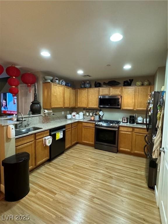 kitchen featuring light wood finished floors, brown cabinets, black appliances, and a sink