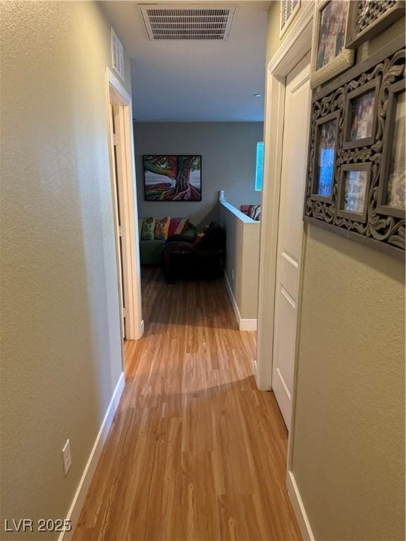 hallway with visible vents, baseboards, and wood finished floors