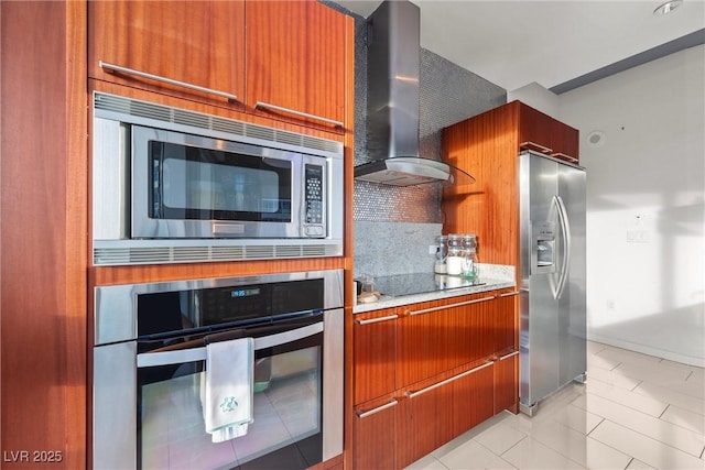 kitchen featuring backsplash, light tile patterned floors, brown cabinets, stainless steel appliances, and wall chimney exhaust hood