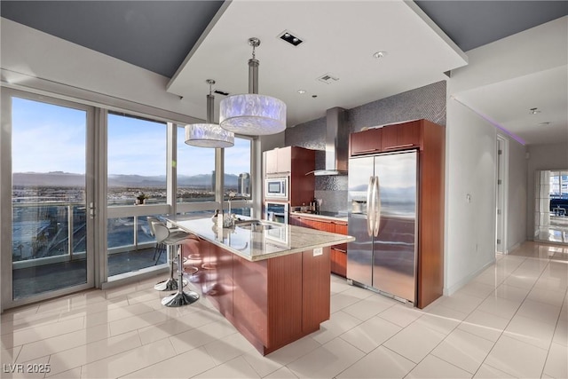 kitchen with a sink, backsplash, appliances with stainless steel finishes, wall chimney exhaust hood, and a healthy amount of sunlight