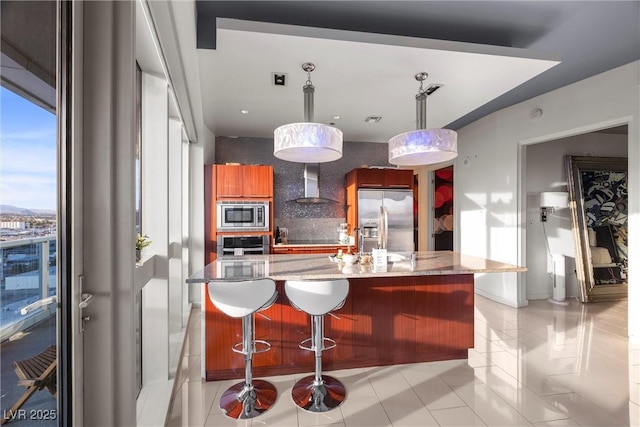 kitchen featuring light stone counters, backsplash, stainless steel appliances, and wall chimney range hood