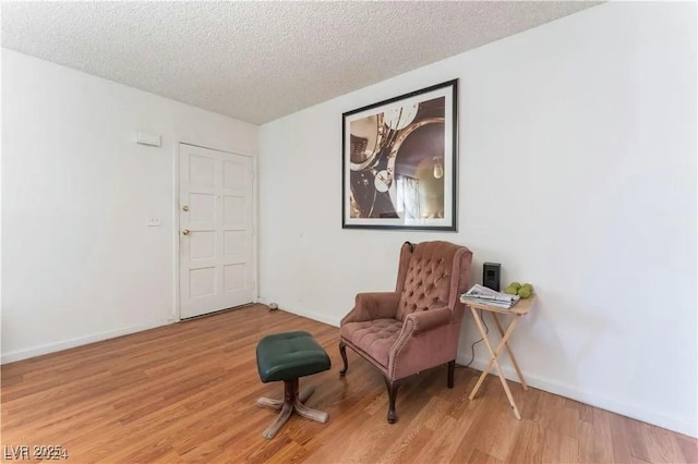 living area featuring light wood-style flooring, a textured ceiling, and baseboards