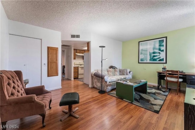 living area featuring baseboards, wood finished floors, visible vents, and a textured ceiling