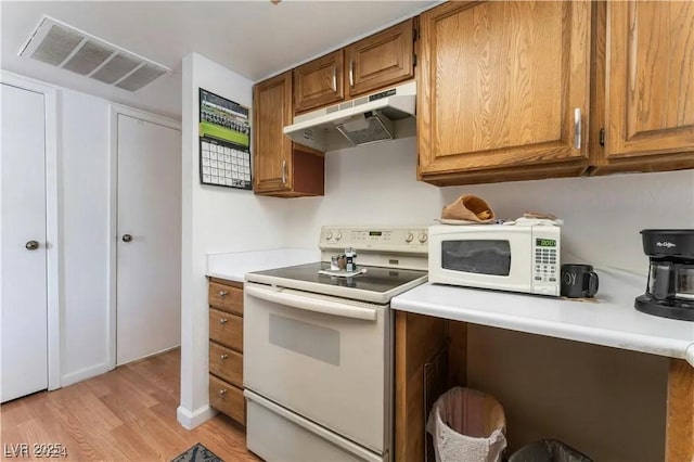 kitchen featuring visible vents, under cabinet range hood, white appliances, brown cabinetry, and light countertops