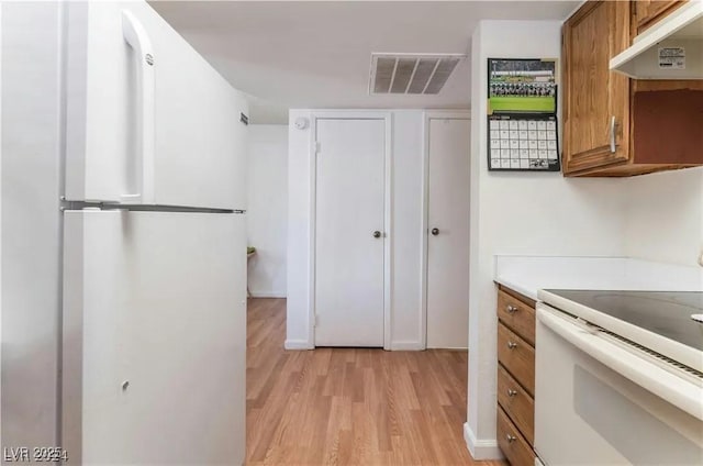 kitchen with under cabinet range hood, visible vents, white appliances, and brown cabinets