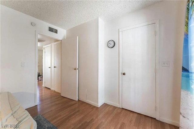 hall with light wood-style floors, visible vents, and a textured ceiling