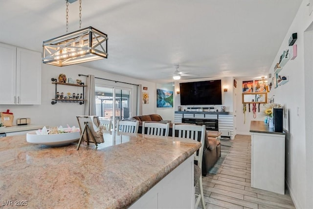 kitchen featuring light stone countertops, pendant lighting, light wood-style floors, white cabinetry, and a ceiling fan