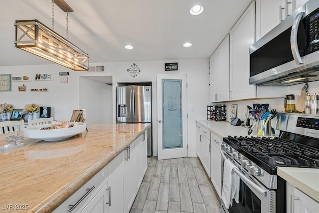 kitchen with wood finish floors, pendant lighting, recessed lighting, appliances with stainless steel finishes, and white cabinets