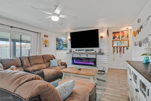 living room featuring a glass covered fireplace, light wood-style flooring, baseboards, and ceiling fan