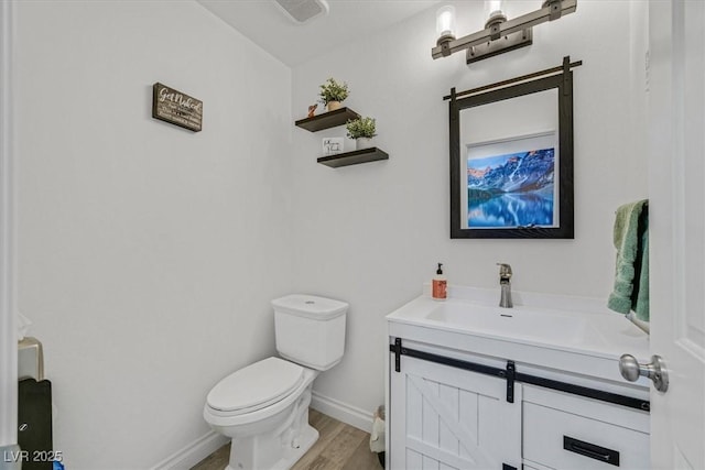 half bathroom with baseboards, toilet, wood finished floors, and vanity