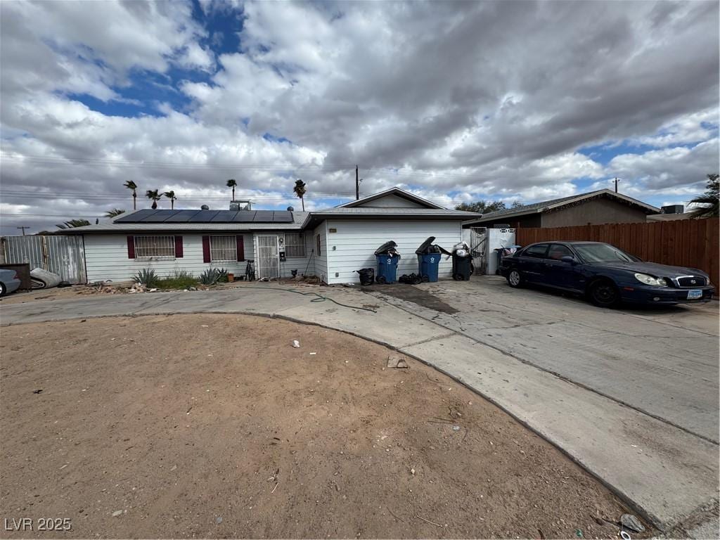 ranch-style house with roof mounted solar panels, driveway, and fence