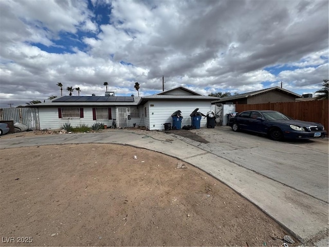 ranch-style house with roof mounted solar panels, driveway, and fence