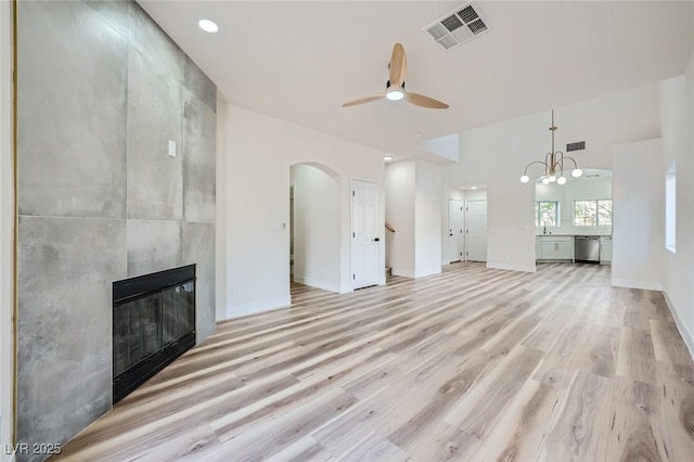 unfurnished living room featuring visible vents, a large fireplace, ceiling fan with notable chandelier, light wood-style floors, and arched walkways