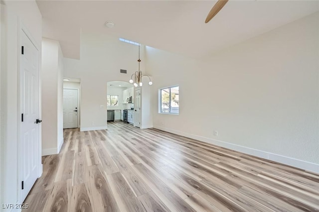 unfurnished living room with visible vents, light wood-style flooring, arched walkways, a high ceiling, and baseboards