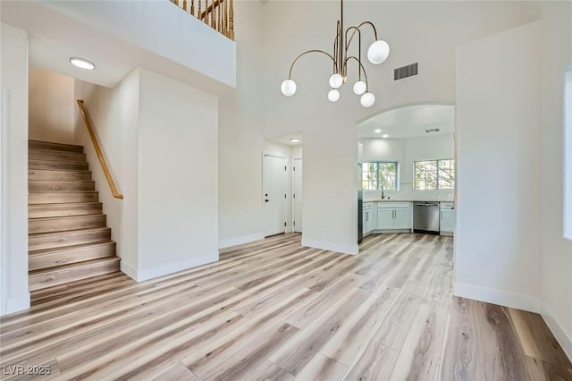 unfurnished living room with baseboards, stairs, a high ceiling, light wood-style floors, and arched walkways