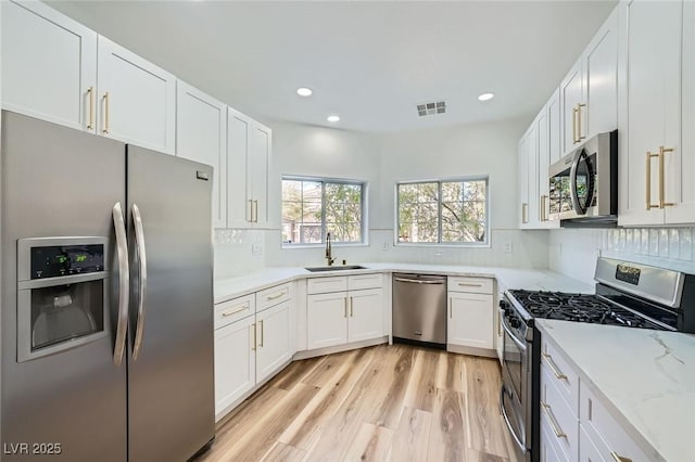 kitchen featuring visible vents, a sink, white cabinetry, appliances with stainless steel finishes, and decorative backsplash