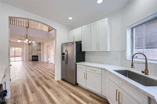 kitchen featuring light stone counters, stainless steel fridge with ice dispenser, a sink, white cabinetry, and light wood-type flooring