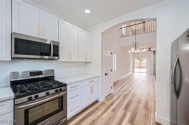 kitchen featuring backsplash, white cabinetry, stainless steel appliances, and an inviting chandelier