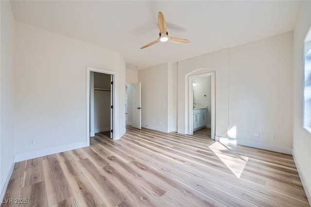 unfurnished bedroom featuring light wood-style floors, baseboards, and arched walkways