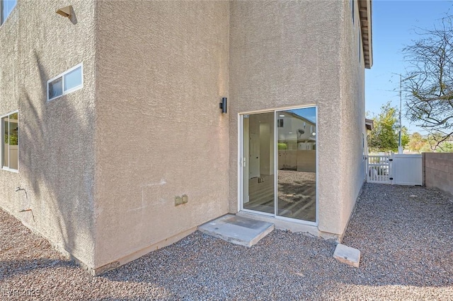 property entrance with stucco siding, fence, and a gate