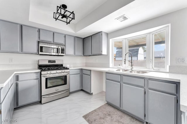 kitchen with visible vents, gray cabinetry, a tray ceiling, stainless steel appliances, and a sink