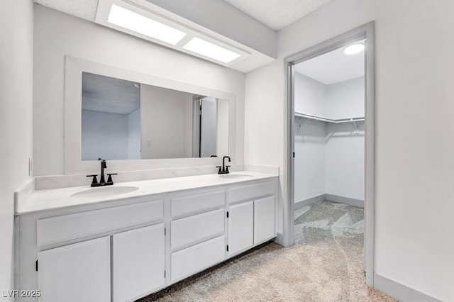 bathroom with double vanity, a walk in closet, baseboards, and a sink