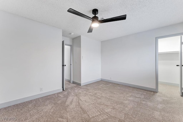 unfurnished bedroom featuring a walk in closet, baseboards, ceiling fan, light colored carpet, and a textured ceiling