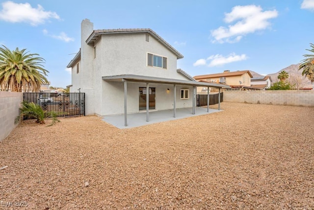 rear view of house with stucco siding, a fenced backyard, a chimney, and a patio area