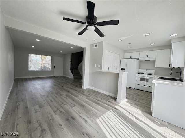 kitchen featuring visible vents, under cabinet range hood, open floor plan, white appliances, and a sink