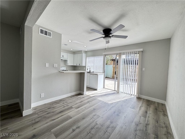 unfurnished living room with visible vents, a ceiling fan, a sink, light wood finished floors, and baseboards