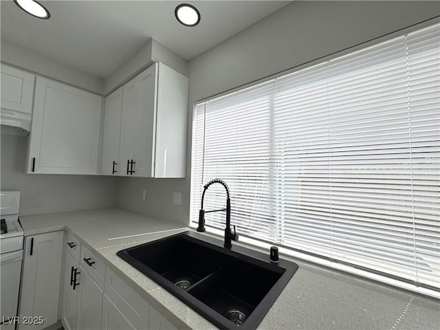 kitchen featuring light stone countertops, under cabinet range hood, stove, white cabinets, and a sink