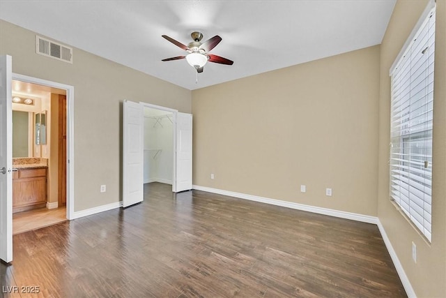 unfurnished bedroom with visible vents, a walk in closet, baseboards, and dark wood-style flooring