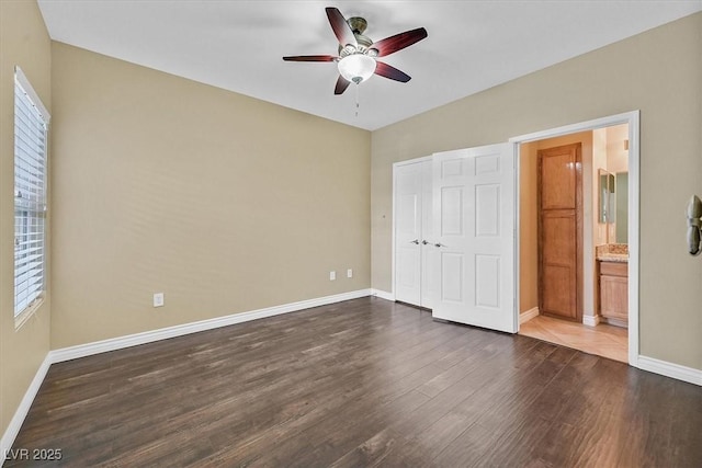 unfurnished bedroom featuring baseboards, dark wood-type flooring, ceiling fan, and ensuite bathroom