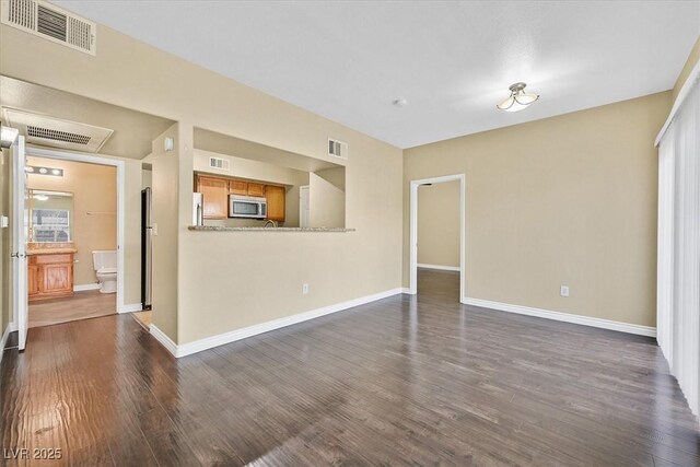 unfurnished living room featuring dark wood finished floors, visible vents, and baseboards