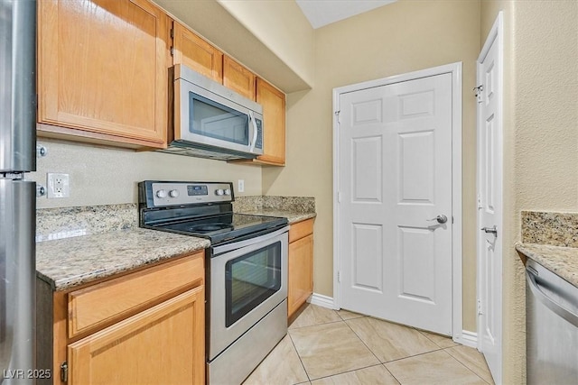 kitchen with light tile patterned flooring, appliances with stainless steel finishes, baseboards, and light stone countertops