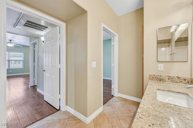 hallway featuring light tile patterned floors, visible vents, baseboards, and a sink