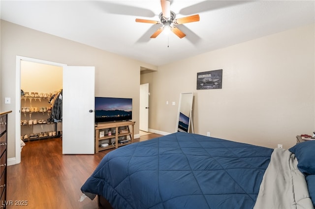 bedroom with baseboards, a walk in closet, a ceiling fan, and wood finished floors