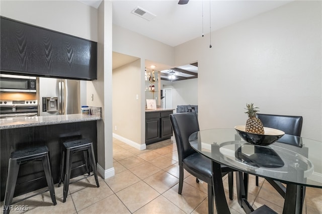 dining room with light tile patterned floors, visible vents, a ceiling fan, and baseboards